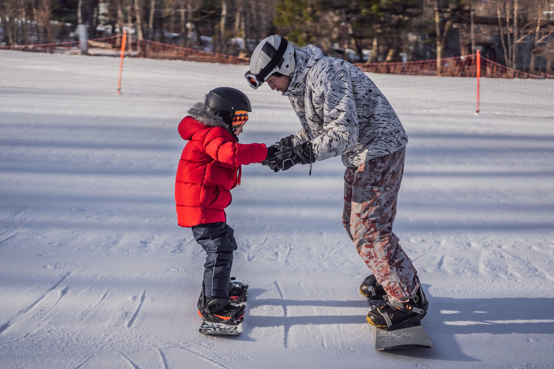 Un homme apprend à son enfant à faire du snowboard.