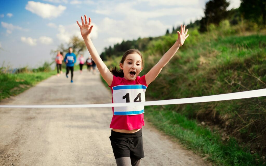 Un enfant lève les bras au ciel en arrivant d'une course à pied.