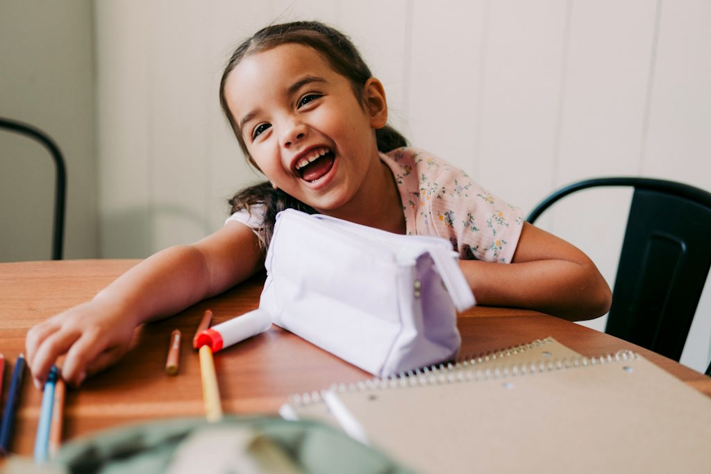 Une enfant sourit à table avec des crayons de couleur.
