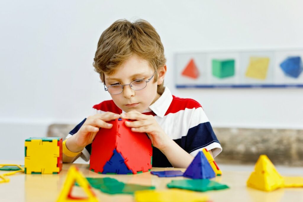 Un garçon avec des lunettes s'amuse à assembler des éléments de plusieurs couleurs.