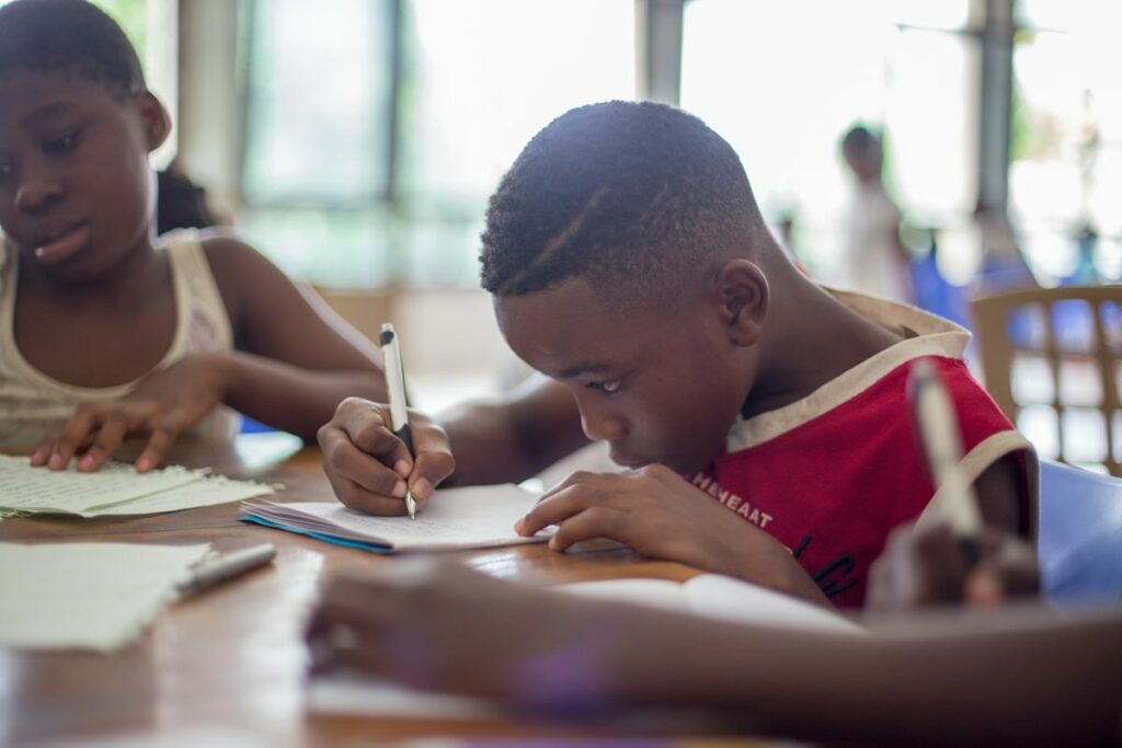 Un enfant vêtu d'un maillot rouge est en train d'écrire sur une feuille de papier.