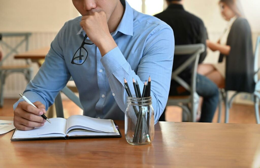 Un jeune homme accoudé à une table, avec un crayon à la main droite.