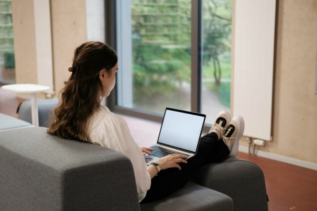 Une jeune femme travaille en ligne, assise sur un canapé gris.
