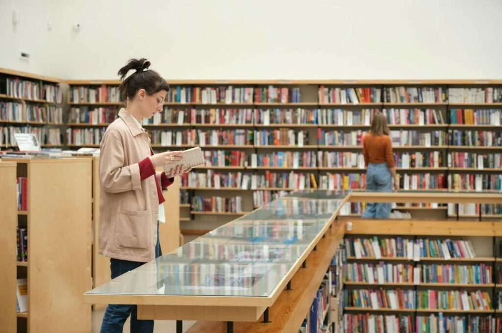 Une étudiante vue de profil en train de lire un livre dans une bibliothèque.