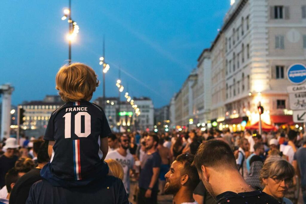 Un petit garçon porte le maillot de football de l'équipe de France, sur les épaules d'un adulte.