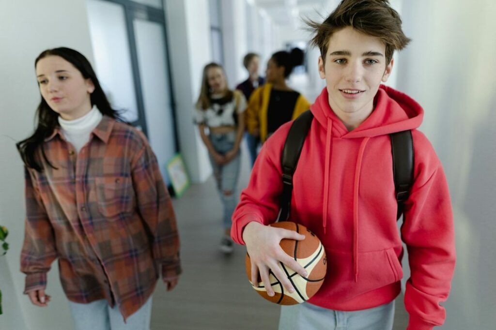 Deux élèves au premier plan, marchent dans un couloir avec un cartable sur le dos.