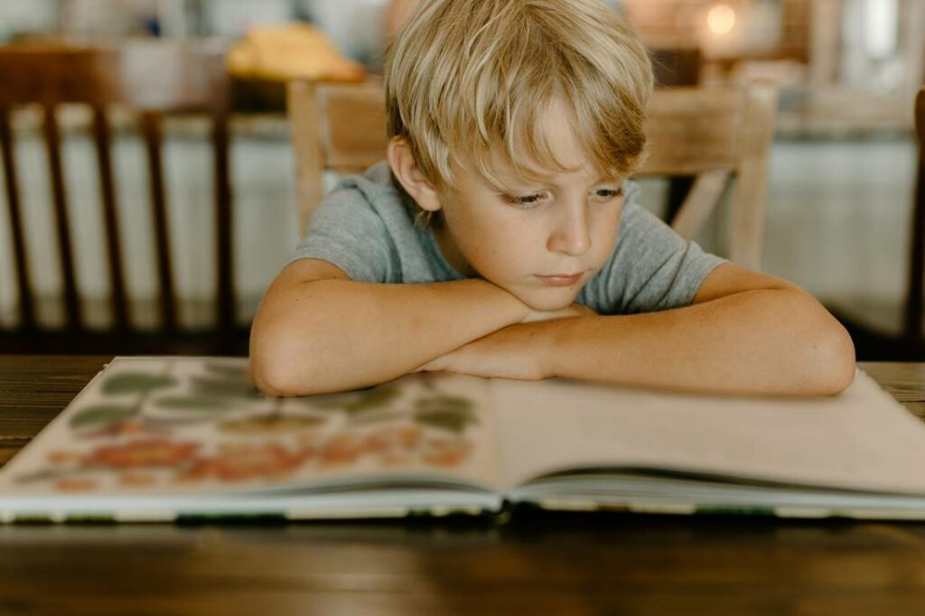 Vue d'un garçon en train de lire un livre, les coudes sur la table.