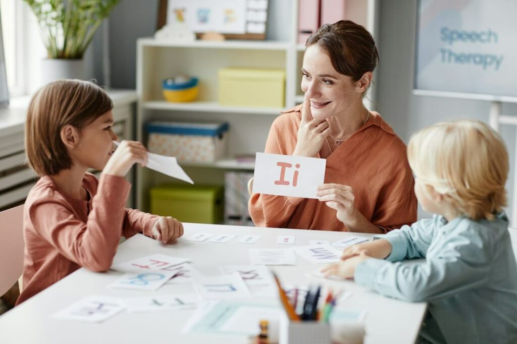 Une mère avec ses deux enfants travaille à prononcer les lettres avec une feuille de papier.