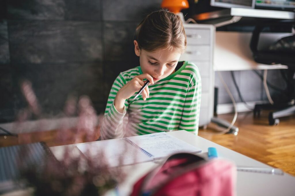 Une fille avec un t-shirt rayé de vert et de blanc lit une feuille avec un crayon à la bouche.