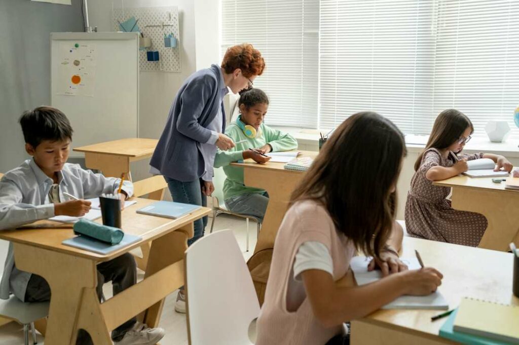 Une enseignante sillonne les rangs de sa classe et corrigeant les travaux d'un élève.