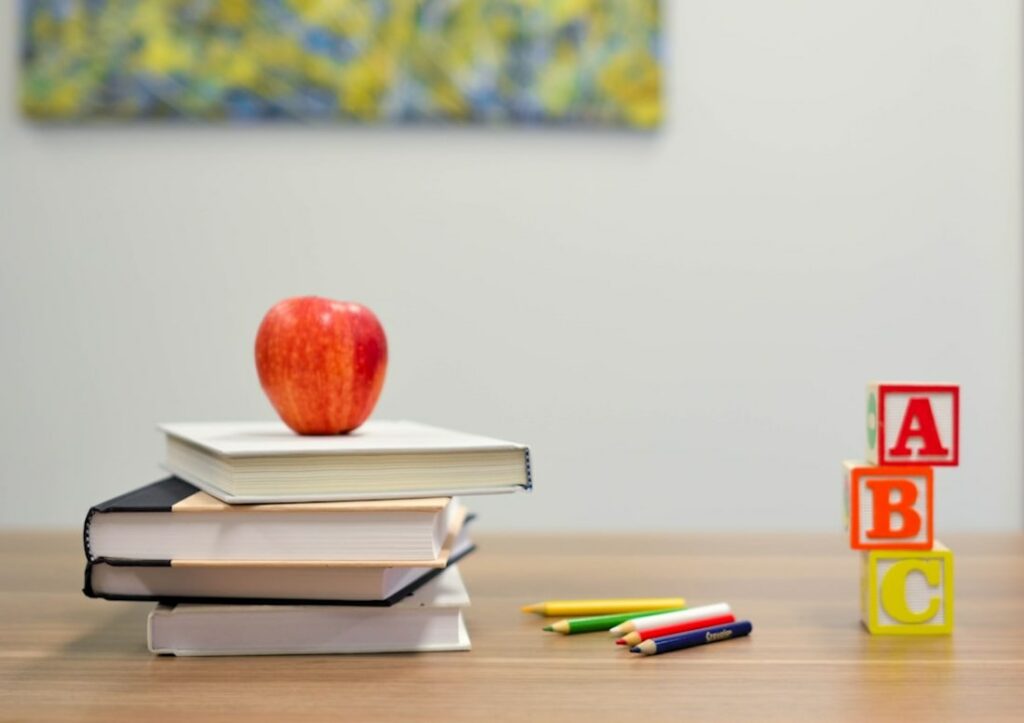 Photo d'une pomme rouge posée sur des manuels sur une table avec des des crayons de couleur.