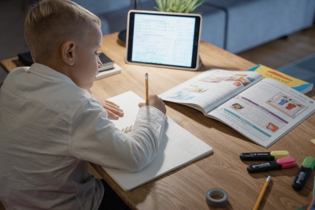 Un garçon écrit sur une feuille de papier devant une tablette.