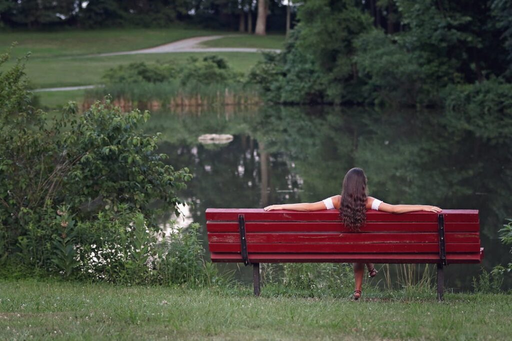 Quelqu'un se repose, assis sur un banc de couleur rouge, au bord d'une étendue d'eau.