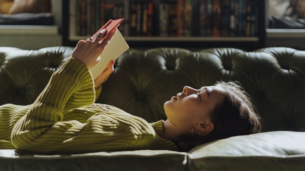 Une femme lit en étant allongée sur un canapé marron.