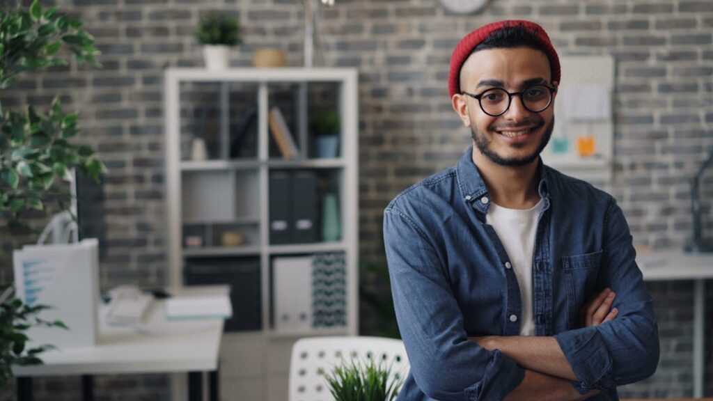 Un homme se tient debout en souriant, les bras croisés dans un salon.