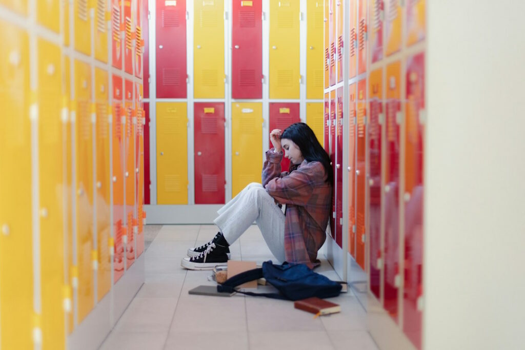 Une étudiante assise au sol, adossée sur des placards scolaires.