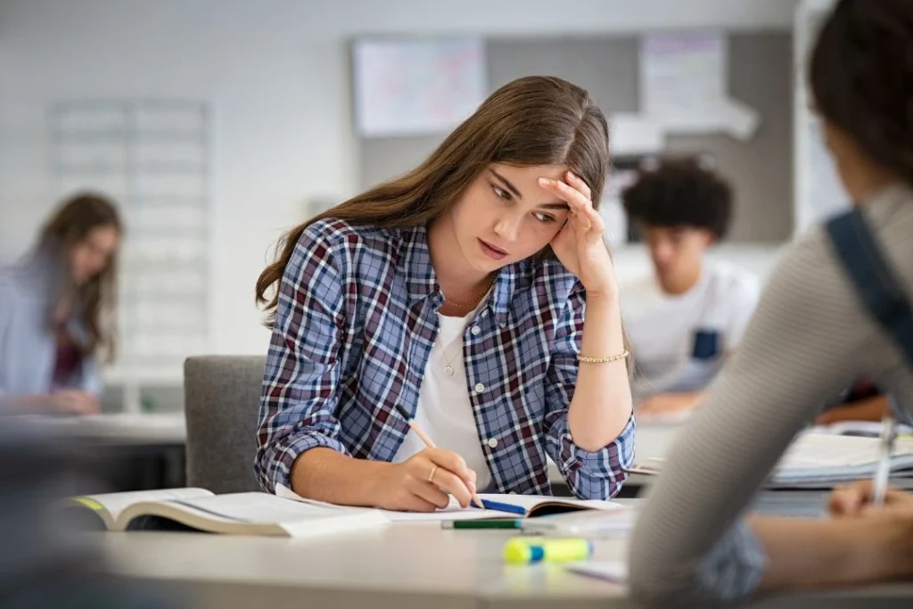 Une jeune femme travaille sur une copie dans une salle de cours.