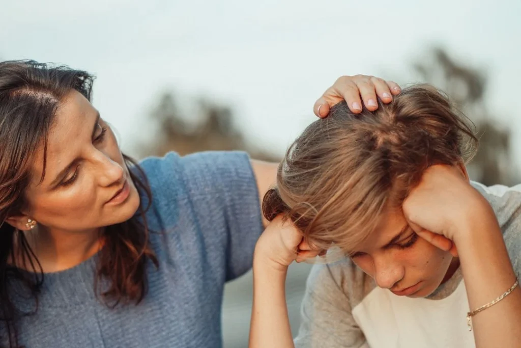 Un jeune garçon semble triste et se fait réconforter par sa mère.