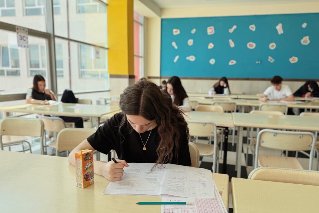 Une élève au premier plan est en train de résoudre un exercice sur table dans une salle de cours.