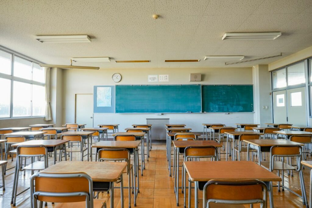 Une salle de cours vide avec tables, chaises et tableau.