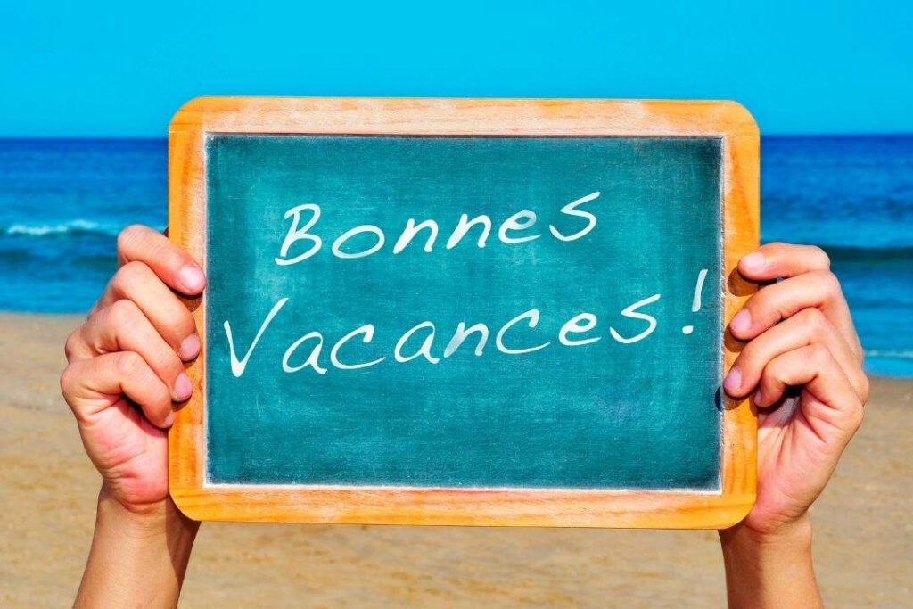 Une personne tient une ardoise sur la plage, avec pour message "bonnes vacances".