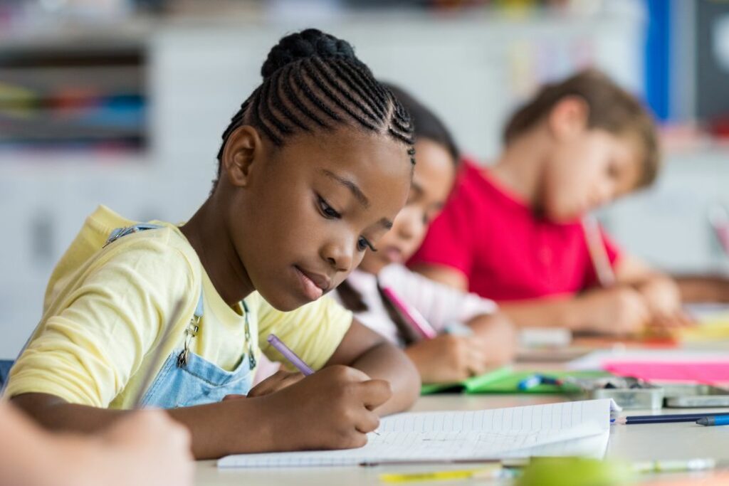 Une fillette est en train d'écrire sur une table à l'école.