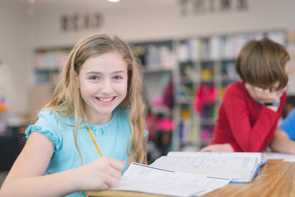 Une jeune élève travaille seule à sa table, dans une salle de cours.
