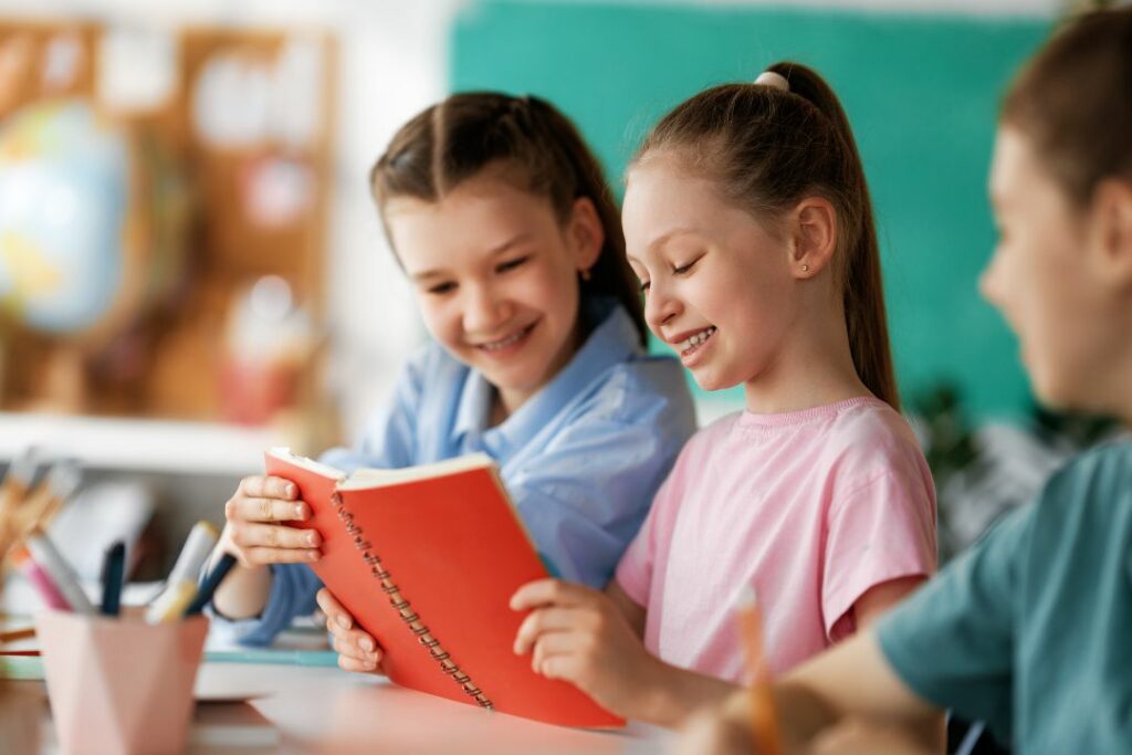 Trois jeunes écolières en train de lire sur un cahier à spirale rouge.