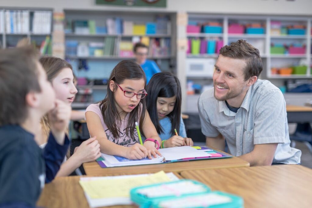 Un homme en chemise donne un cours à des écoliers dans une bibliothèque.