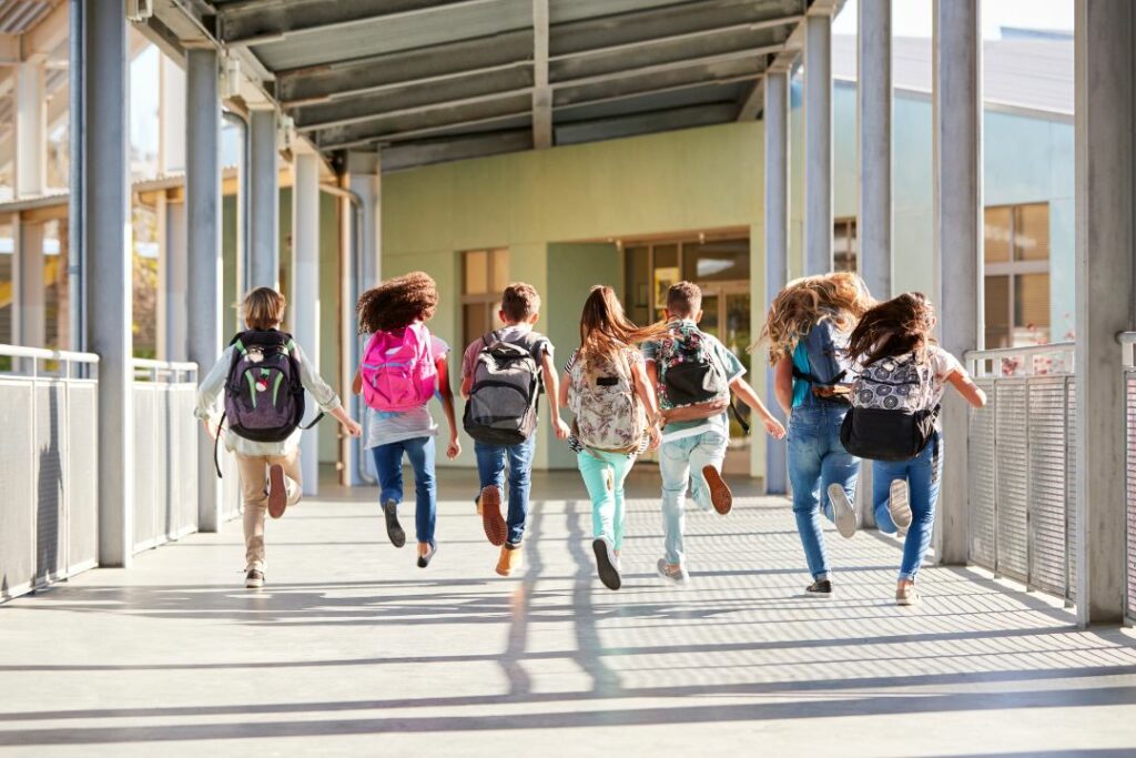 Un groupe d'enfants est en train de courir dans un couloir avec leur cartable sur le dos.