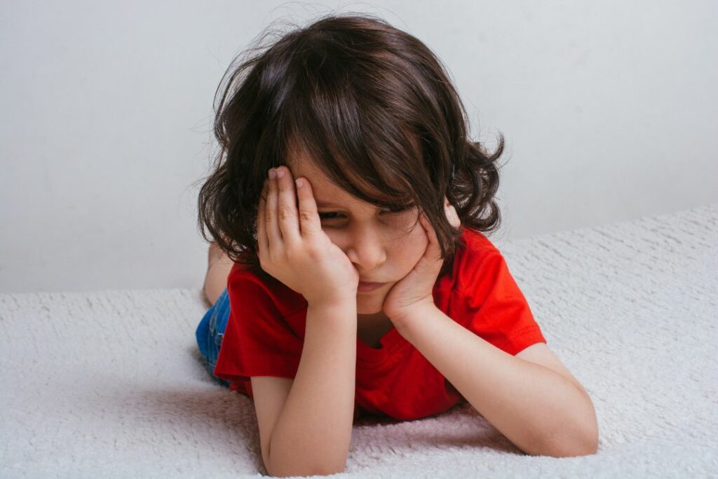 Un petit garçon se tient la tête dans ses mains et semble triste.