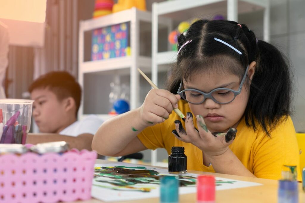 Une jeune élève est en train de se peindre les doigts dans une salle de classe.