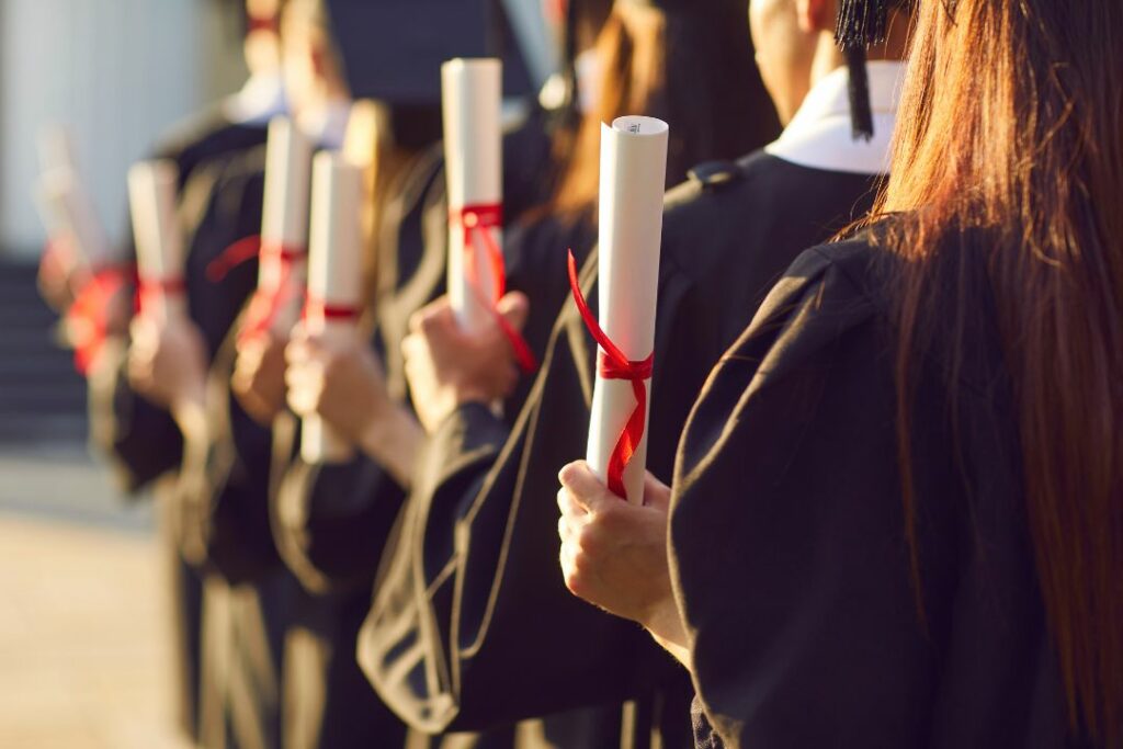 Rangée d'étudiants en toge tenant leurs diplômes enroulés avec un ruban rouge lors d'une cérémonie de remise.