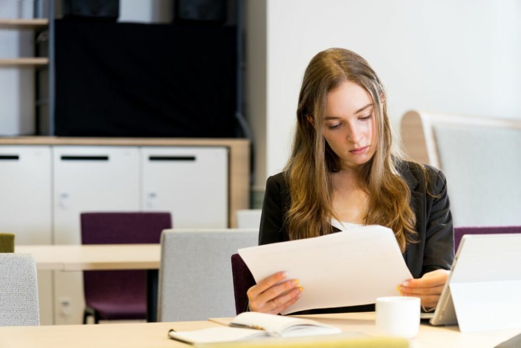 Jeune femme concentrée lisant des documents à son bureau dans un espace de travail moderne.